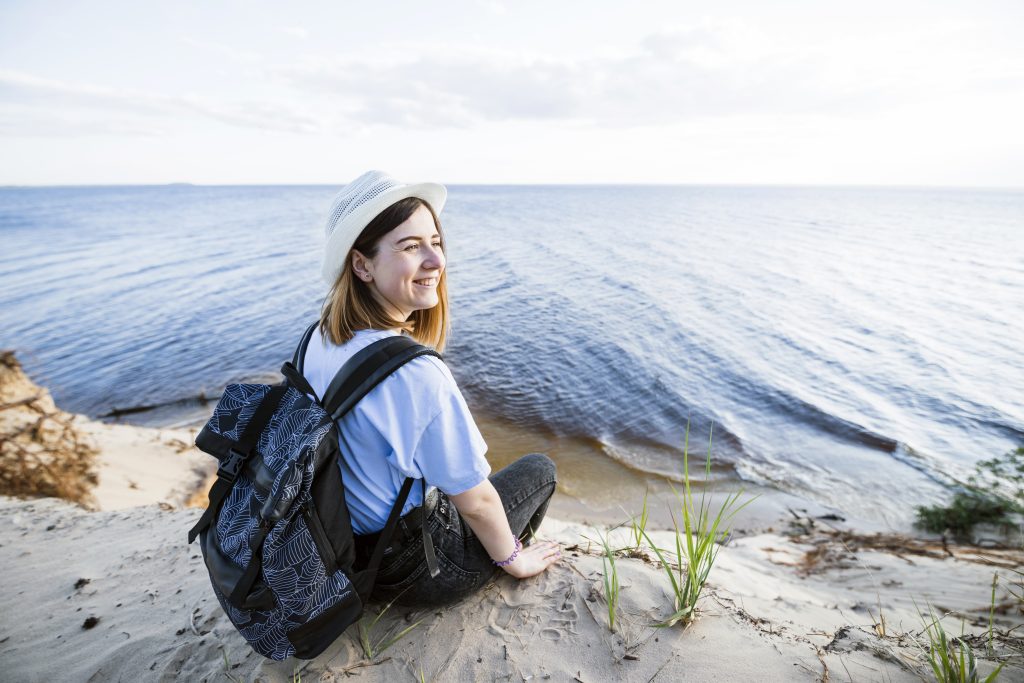 A solo traveler, dressed warmly in a yellow jacket and backpack, stands at the edge of a snow-covered cliff, overlooking a calm winter town and a river. The scene captures the serenity and excitement of solo travel during winter, symbolizing adventure, exploration, and personal freedom.